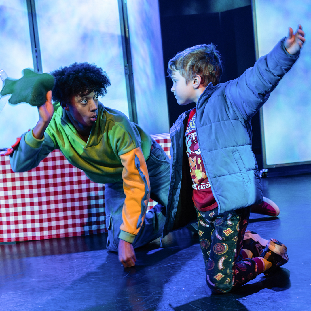 An actor in Dinosaur! interacting with a small child live on stage.